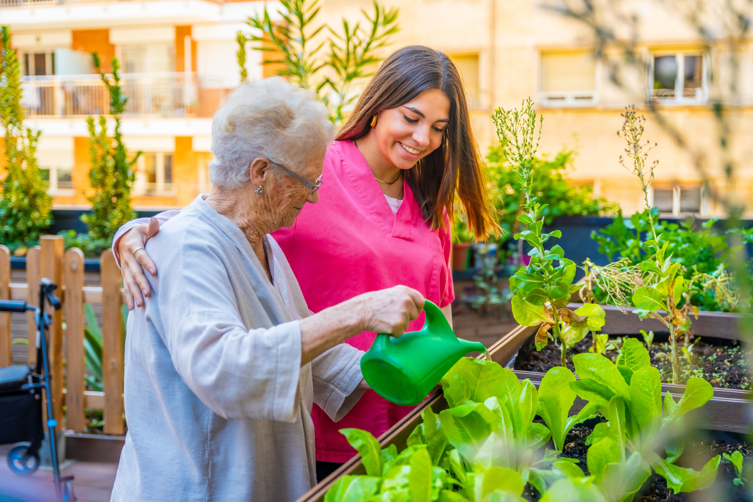 Woman and nurse watering plants in a garden at geriatric